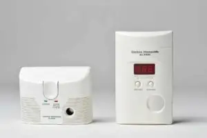 Two types of carbon monoxide alarms on a plain background, one with a digital display and another with a test button and led indicators.